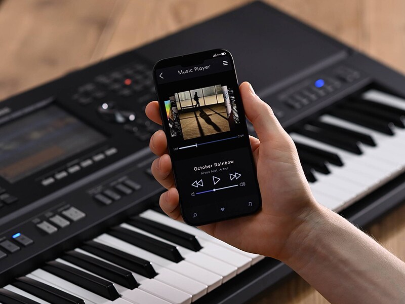 Yamaha Arranger Workstation PSR-SX920 and a hand holding a smartphone with a music player screen