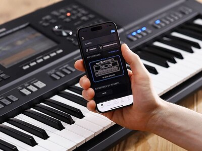 Yamaha Arrange Workstation PSR-SX920 and a hand holding a smartphone with the Yamaha official app “Expansion Explorer” screen