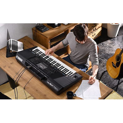 Photo of a person writing on sheet music while playing the Yamaha Arranger Workstation PSR-SX720