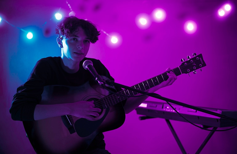 Person playing a F310 acoustic guitar on stage with ambient lights behind them.