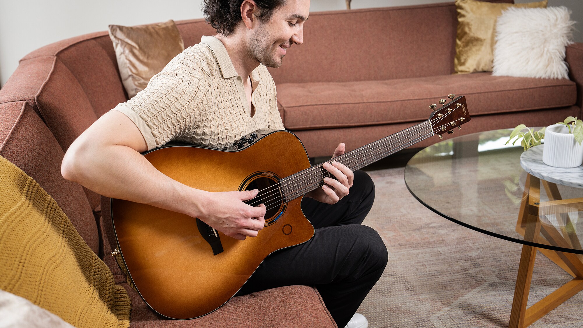 A man sitting on a sofa in the living room playing a TAG3 C acoustic guitar