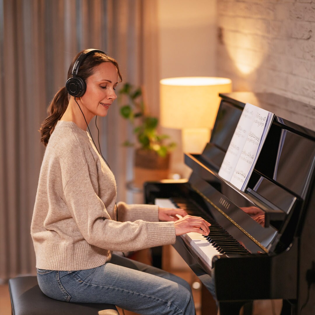 A woman enjoys playing the piano while wearing headphones
