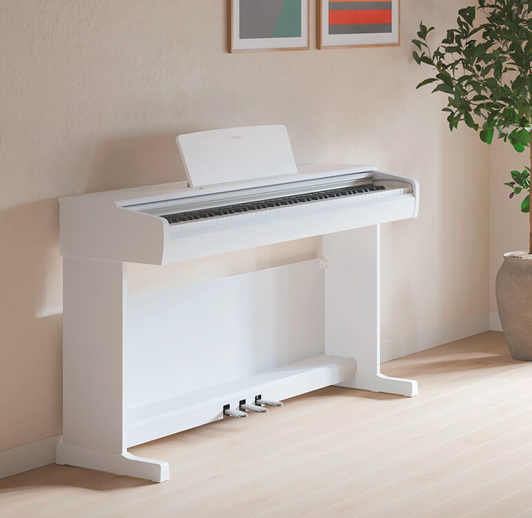 A living room featuring a white ARIUS piano with houseplants and a sofa, harmoniously integrated with the interior