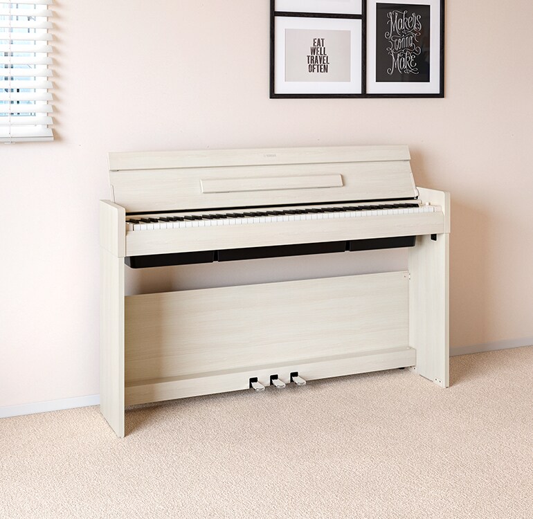 A living room featuring a White Birch ARIUS piano positioned next to wall shelves with lamps and a diffuser, blending harmoniously with the interior.